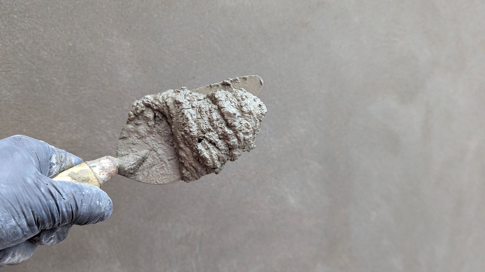 Close-up of a hand holding a trowel with cement, perfect for construction themes.